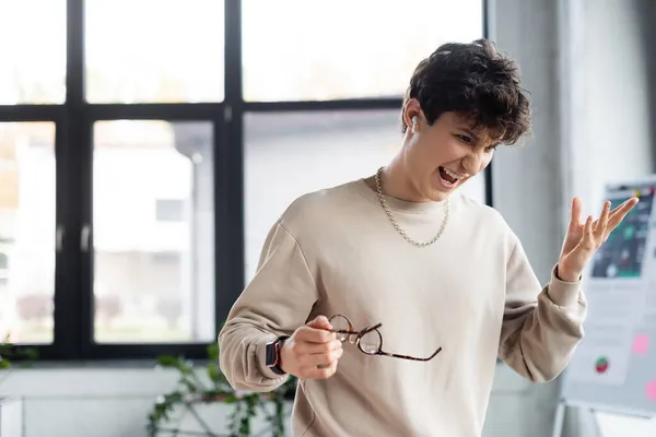 Homme d'affaires en colère dans l'écouteur tenant des lunettes dans le bureau — Photo de stock