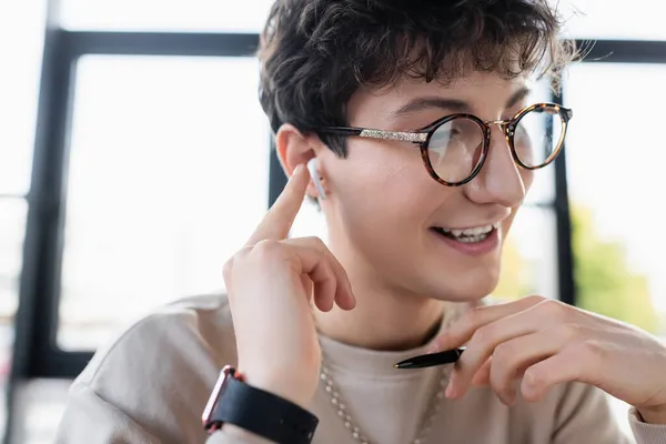 Joven transexual en gafas y auriculares con bolígrafo en la oficina - foto de stock