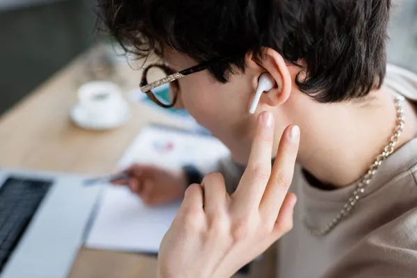 Hombre de negocios en auriculares que trabajan cerca de ordenador portátil borroso en la oficina - foto de stock