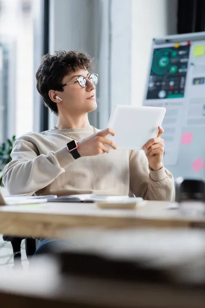 Transgender person in earphone and eyeglasses holding digital tablet in office — Stock Photo