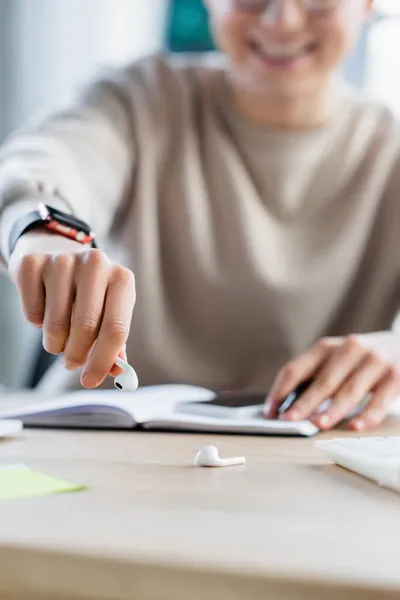 Vista ritagliata di uomo d'affari offuscata prendendo auricolare vicino calcolatrice e notebook in ufficio — Foto stock