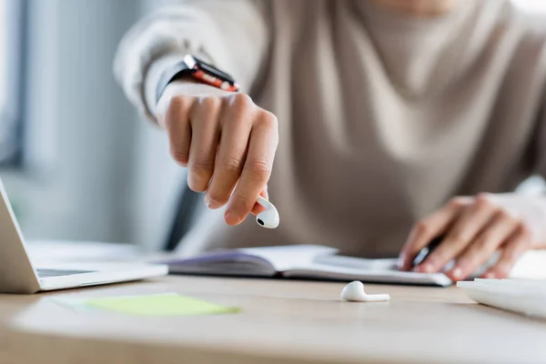 Cropped view of businessman taking wireless earphone near laptop and calculator in office — Stock Photo