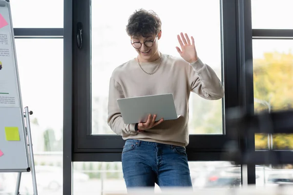 Smiling transgender person having video call on laptop near flip chart in office — Stock Photo