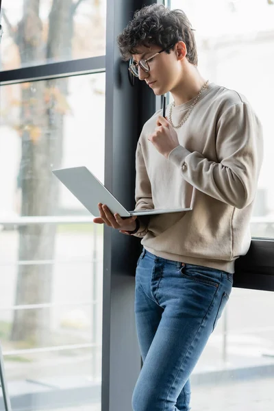 Молодой бизнесмен держит ручку и ноутбук у окна в офисе — стоковое фото