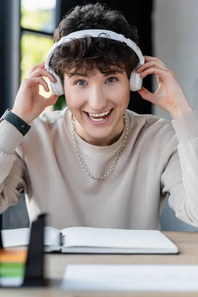 Une personne transgenre positive dans un casque regardant une caméra près d'un ordinateur portable flou au bureau — Photo de stock