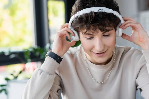 Smiling young transgender person using headphones in office — Stock Photo