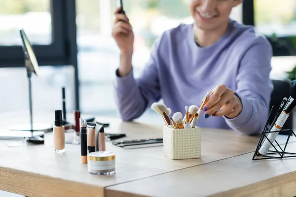 Vista cortada de cosméticos decorativos perto de pessoa transgênero borrada em estúdio — Fotografia de Stock