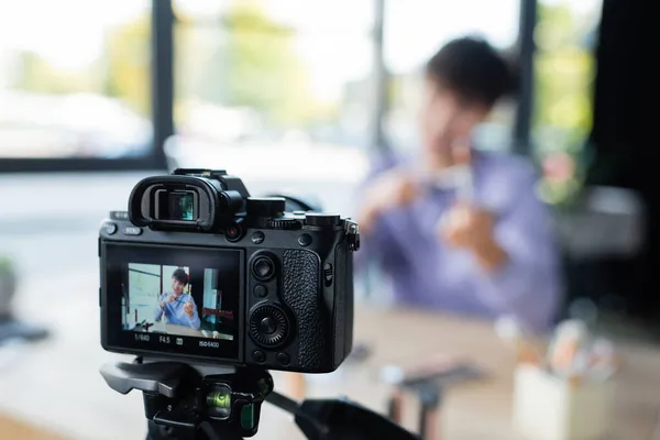 Digital camera on tripod near blurred transgender person with cosmetic brushes — Stock Photo