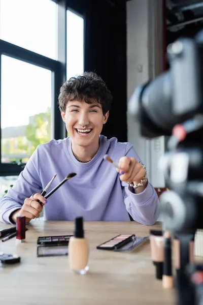 Positive transgender blogger looking at digital camera near blurred cosmetics — Stock Photo