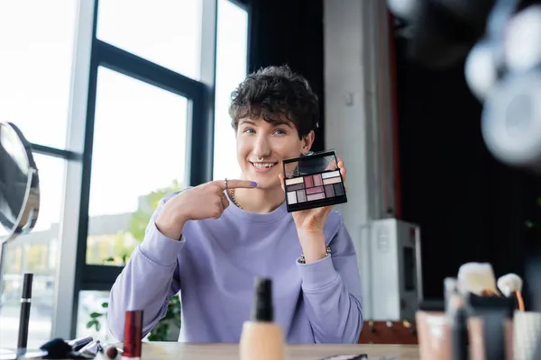Smiling transgender makeup artist pointing at eye shadows — Stock Photo