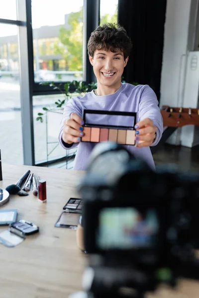 Smiling transgender makeup artist showing eye shadows at digital camera — Stock Photo