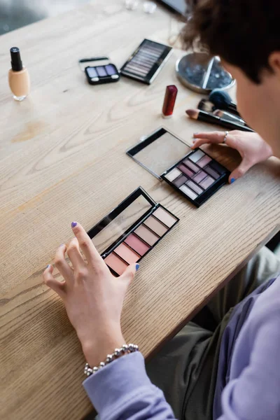 Blurred transgender person holding eye shadows near cosmetics on table — Stock Photo