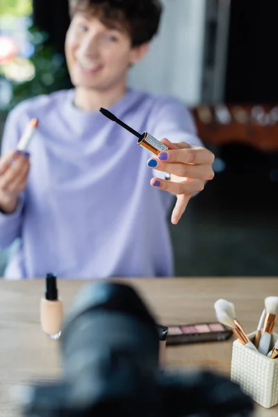 Mascara in der Hand einer verschwommenen Transgender-Person in der Nähe der Digitalkamera — Stockfoto