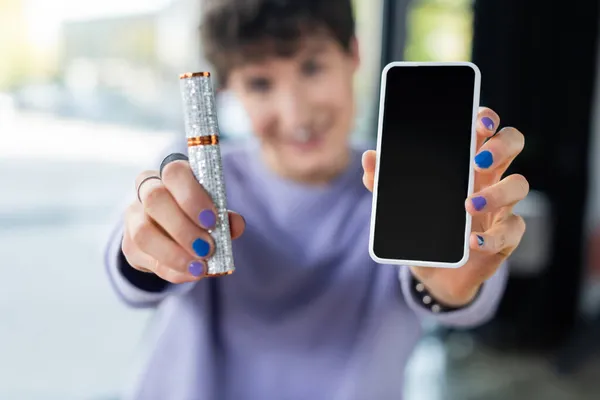 Smartphone and mascara in hands of blurred transgender person — Stock Photo