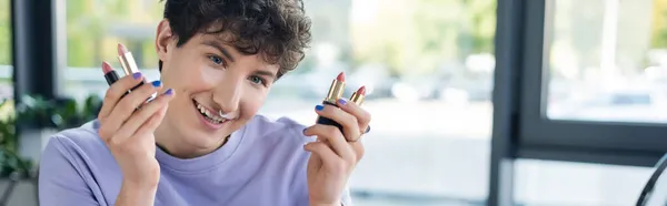 Smiling transgender person holding lipsticks, banner — Stock Photo
