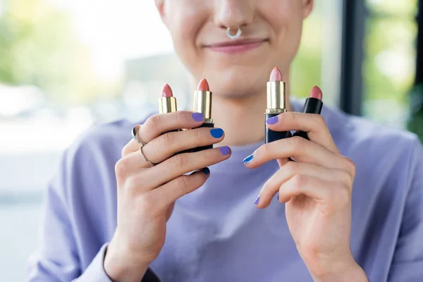 Vue recadrée des rouges à lèvres dans les mains d'une personne transgenre souriante — Photo de stock