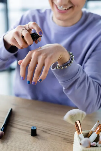 Vue recadrée de la personne transgenre gaie versant le fond de teint sur la main près des pinceaux cosmétiques — Photo de stock