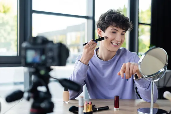 Positivo transgender persona che applica fondazione volto vicino specchio e fotocamera digitale offuscata — Foto stock