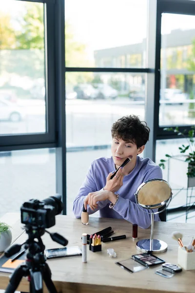 Transgender person applying makeup foundation near cosmetics and digital camera in studio — Stock Photo