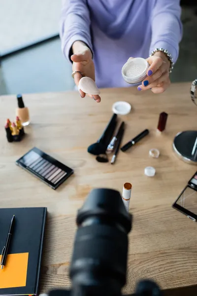 Vista recortada de la persona transgénero sosteniendo polvo facial cerca de la cámara digital y cosméticos decorativos - foto de stock