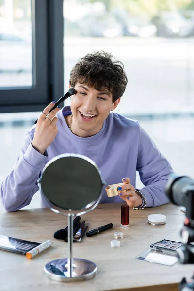 Sorrindo transgênero pessoa aplicando pó facial perto de espelho, cosméticos decorativos e câmera digital — Fotografia de Stock