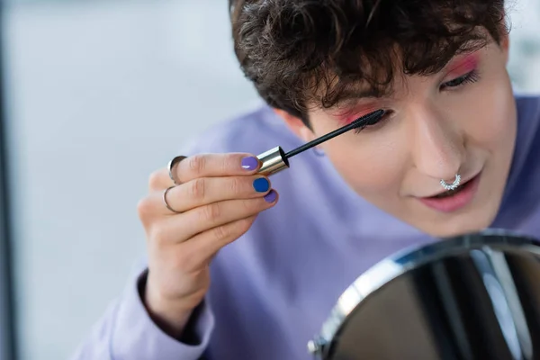 Young transgender person applying mascara near blurred mirror — Stock Photo