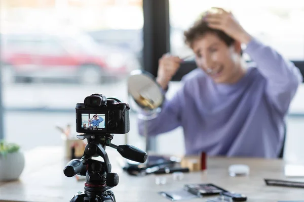 Digital camera near blurred transgender person with cosmetic brush and decorative cosmetics — Stock Photo