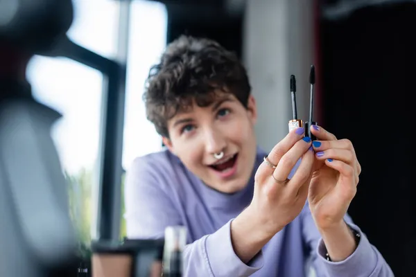 Mascara brushes in hands of blurred transgender person near digital camera — Stock Photo