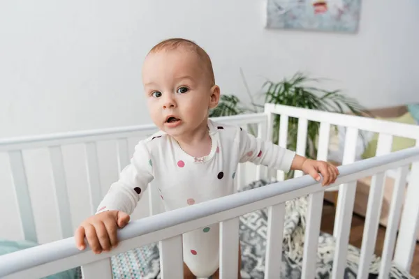 Little child looking at camera while standing in baby crib — Stock Photo