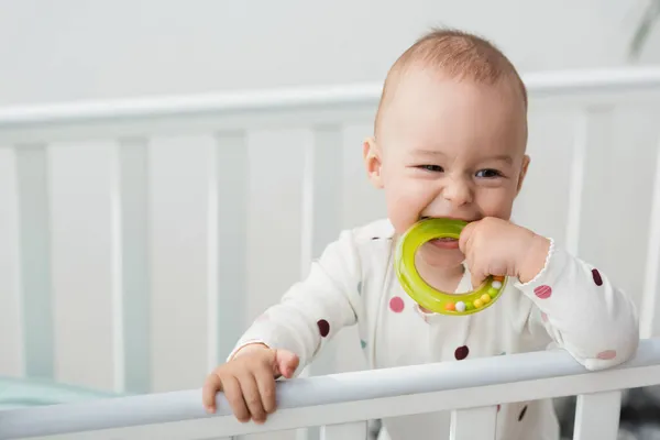 Fröhliches Kleinkind beißt Rasselring im Kinderbett — Stockfoto