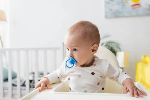 Toddler kid with pacifier sitting in baby chair — Stock Photo