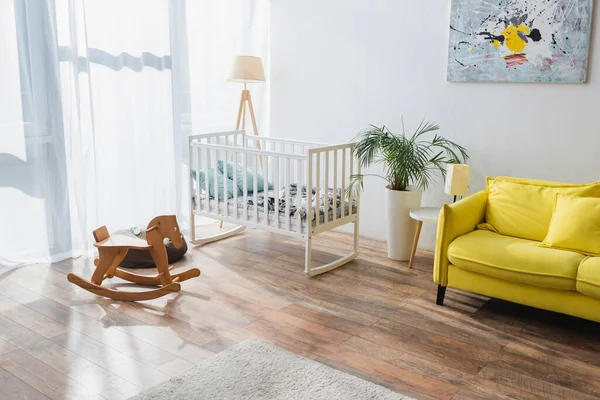 Spacious room with yellow sofa, baby crib and rocking horse — Stock Photo