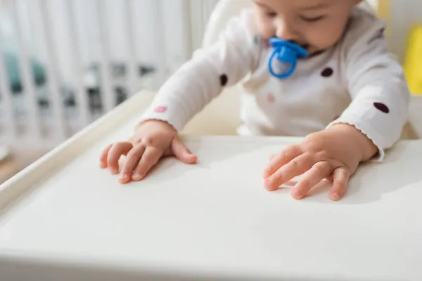 Menino borrado com chupeta sentado em cadeira de bebê — Fotografia de Stock