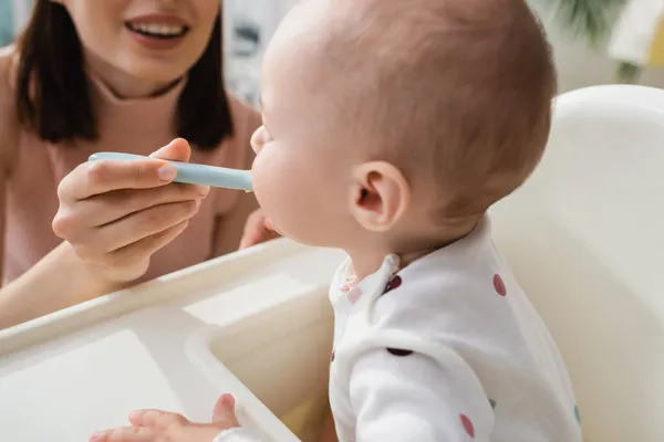 Blurred woman smiling while feeding little kid at home — Stock Photo
