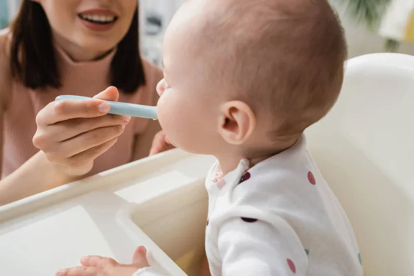 Donna sfocata sorridente durante l'alimentazione del bambino a casa — Foto stock