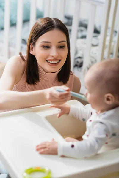 Cheerful woman feeding blurred son from spoon at home — Stock Photo