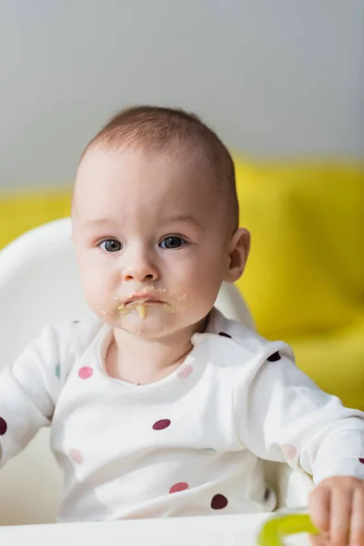 Criança com alimentos em lábios sentados em cadeira de bebê — Fotografia de Stock