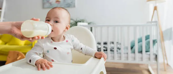 Tout-petit garçon boire du lait tout en étant assis dans la chaise de bébé, bannière — Photo de stock