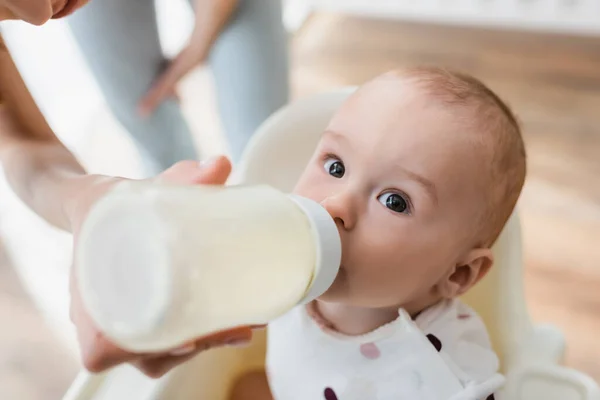 Високий кут зору хлопчика, який п'є молоко з дитячої пляшки поблизу розмитої мами — стокове фото
