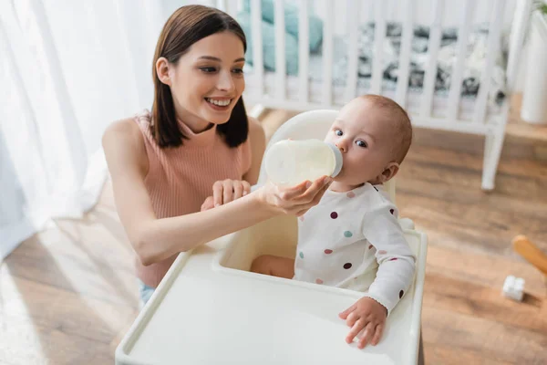 Alto ângulo vista de feliz morena mulher alimentando filho com leite em casa — Fotografia de Stock