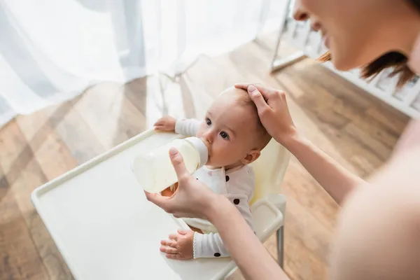 Blurred woman touching head of baby boy while feeding him with milk — Stock Photo