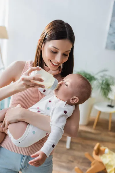 Sorridente donna bruna che alimenta il figlio del bambino con il latte a casa — Foto stock