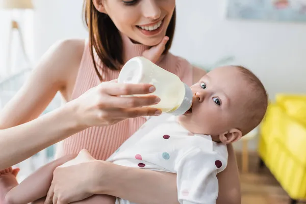 Розмита жінка посміхається під час годування маленького сина з дитячої пляшки — стокове фото