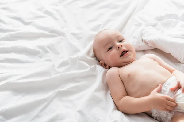 Bambino in pannolini sdraiato su biancheria da letto bianca e guardando la fotocamera — Foto stock