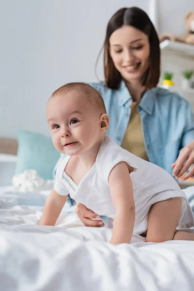 Toddler boy in romper crawling on bed near blurred mother — Stock Photo