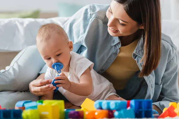 Smiling woman with baby boy playing with blurred building blocks on floor — Stock Photo