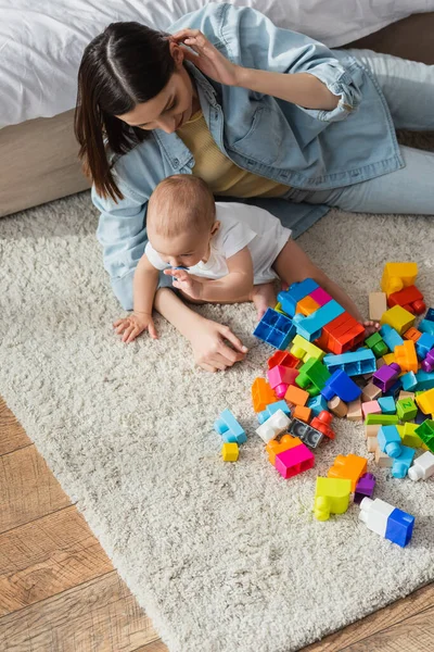 High angle view of brunette woman and her little son playing with building blocks on floor carpet — Stock Photo
