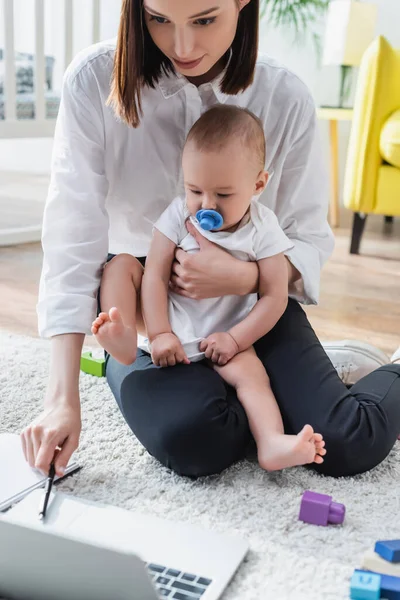 Donna seduta sul pavimento con il piccolo figlio mentre tiene la penna vicino al taccuino sfocato — Foto stock