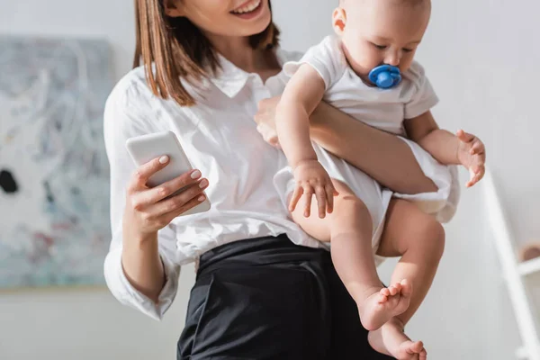 Blurred woman holding smartphone and little son in romper — Stock Photo