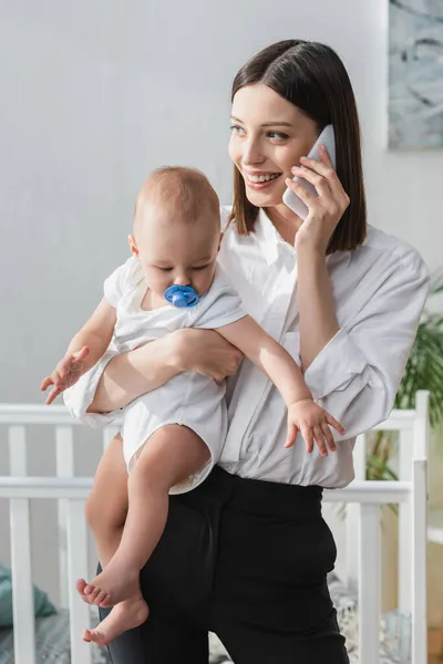 Donna sorridente che parla sullo smartphone mentre tiene in mano il bambino — Foto stock